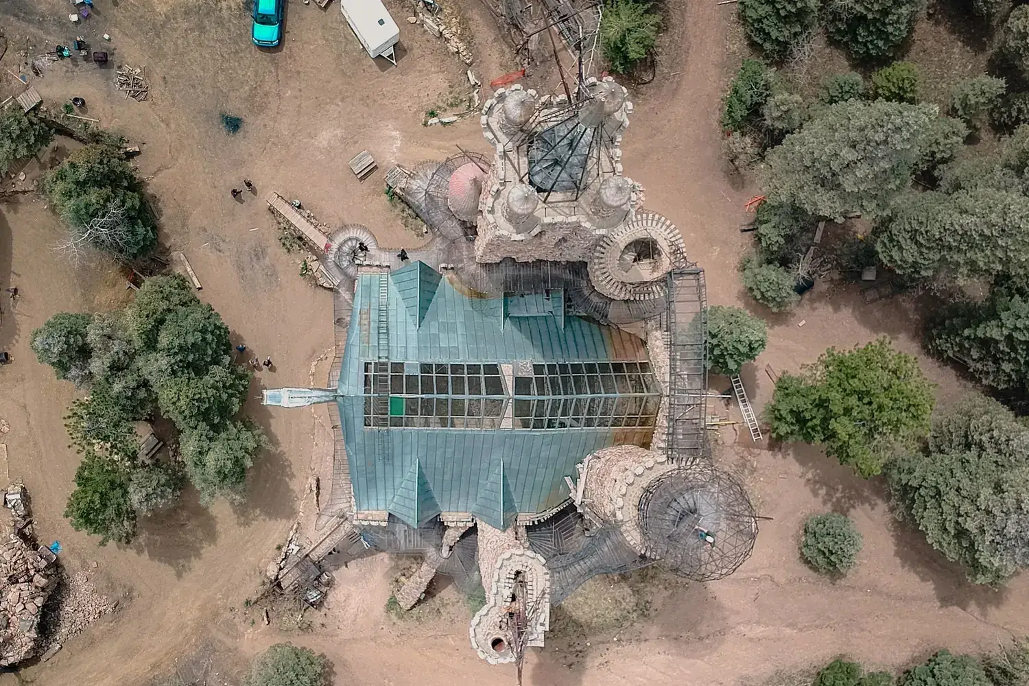 Top-down drone view of a stone building with a green roof, surrounded by tracks, vehicles and trees